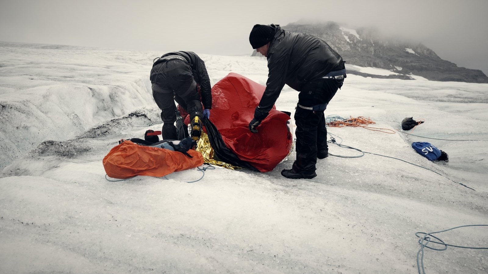 Zwei Einsatzkräfte versorgen einen Verletzten im Biwaksack auf einem Gletscher