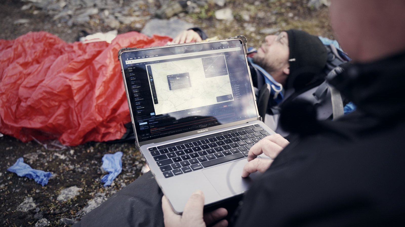 Laptop mit Patientenbild neben einem Patienten im Biwaksack